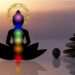 Silhouette of a person meditating with seven colored chakras aligned, sunrise background, and balanced zen stones.