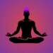 Silhouette of a person meditating in lotus position with a glowing crown chakra on top of the head, set against a purple and pink gradient background.