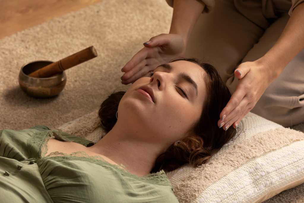 "Reiki practitioner performing energy healing on a woman lying down with eyes closed, creating a calm and relaxing environment."