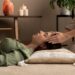 Reiki therapist placing hands on a woman's head during an energy healing session in a peaceful room with candles and a Himalayan salt lamp.