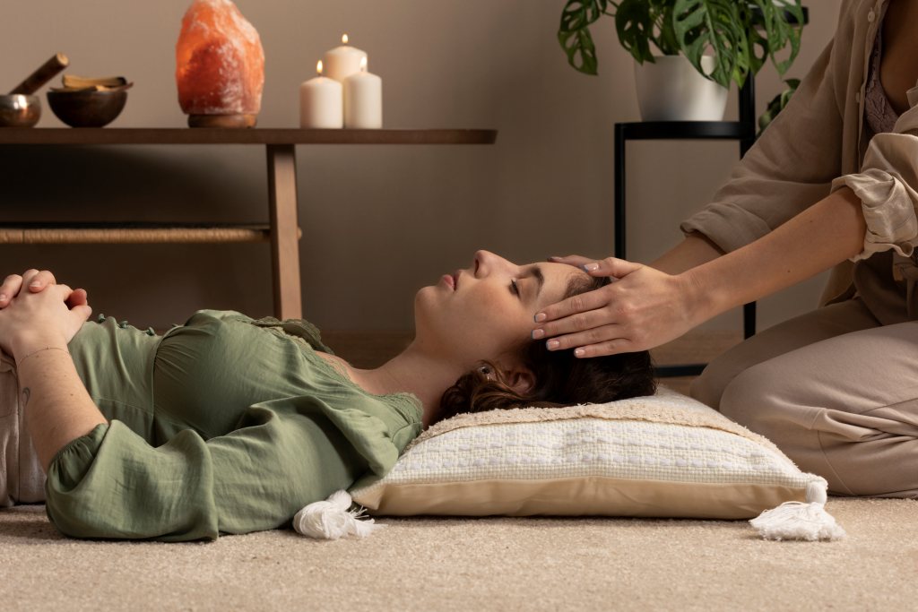 "Reiki therapist placing hands on a woman's head during an energy healing session in a peaceful room with candles and Himalayan salt lamp."