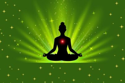 Silhouette of a person meditating with a glowing red heart chakra on a green starry background.